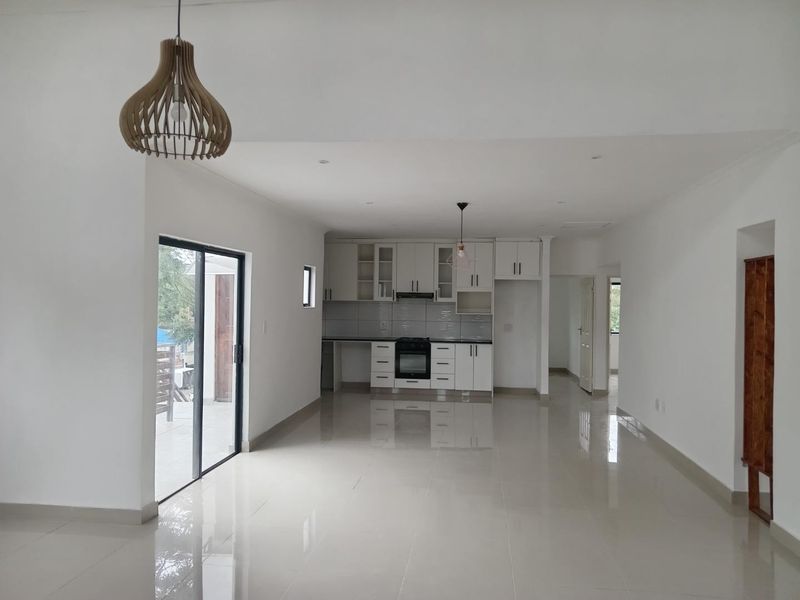 Spacious open-plan living and kitchen area featuring modern white cabinetry, integrated appliances, sleek tiled flooring, and large sliding doors leading to the outdoors.