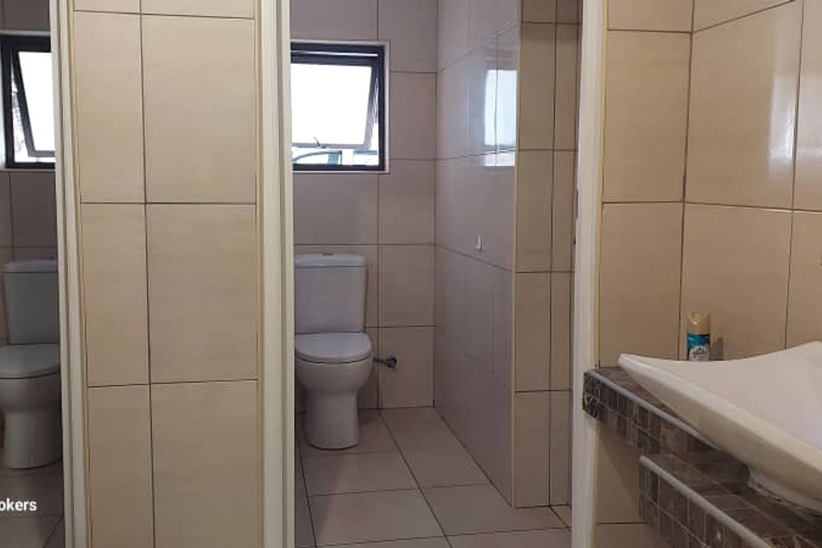 A functional commercial restroom facility featuring two private toilet cubicles and a modern basin with a chrome mixer tap.