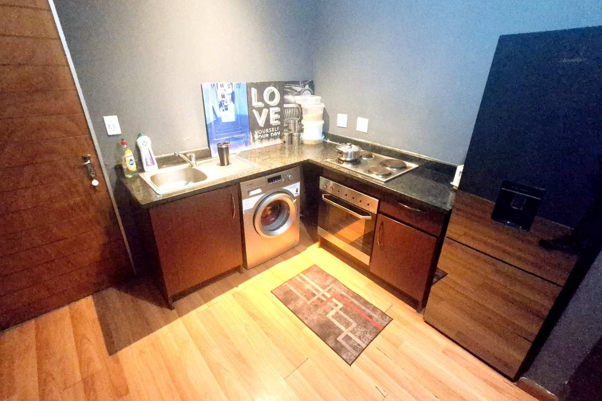 Compact kitchen featuring dark wood cabinetry, granite countertops, built-in oven, electric hob, and an integrated washing machine.