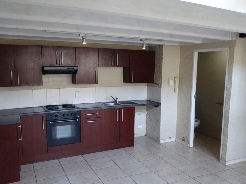 A functional kitchen featuring dark wood cabinetry, built-in oven and hob, tiled flooring, and exposed ceiling beams, with an adjacent bathroom entrance.