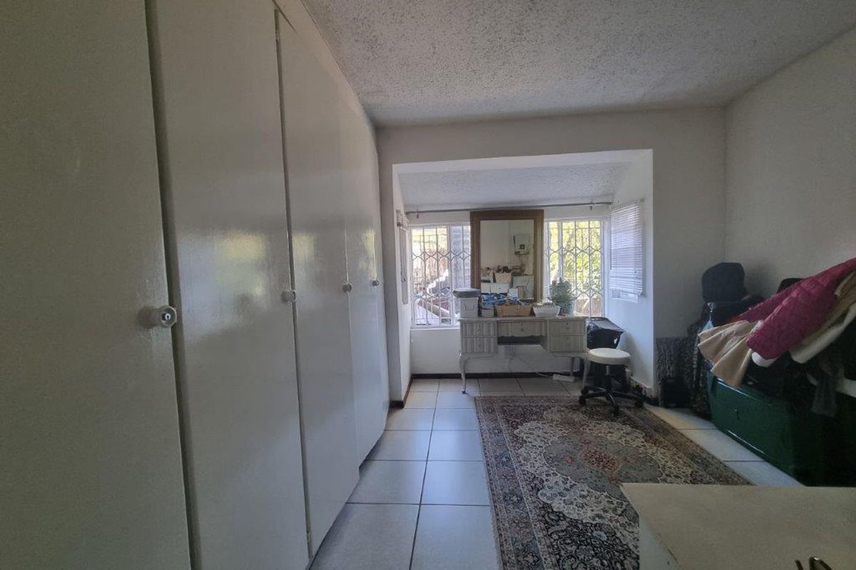 A bedroom featuring built-in floor-to-ceiling cabinetry, tiled flooring, and large windows with security bars, offering a functional layout with natural light.
