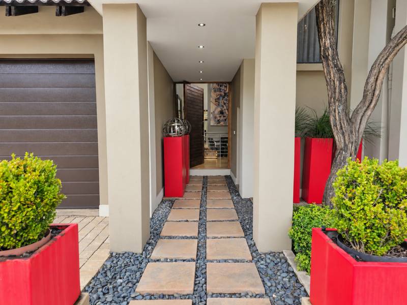 A modern entrance featuring a paved walkway with pebble accents, recessed lighting, and a timber pivot front door adjacent to a sectional garage.