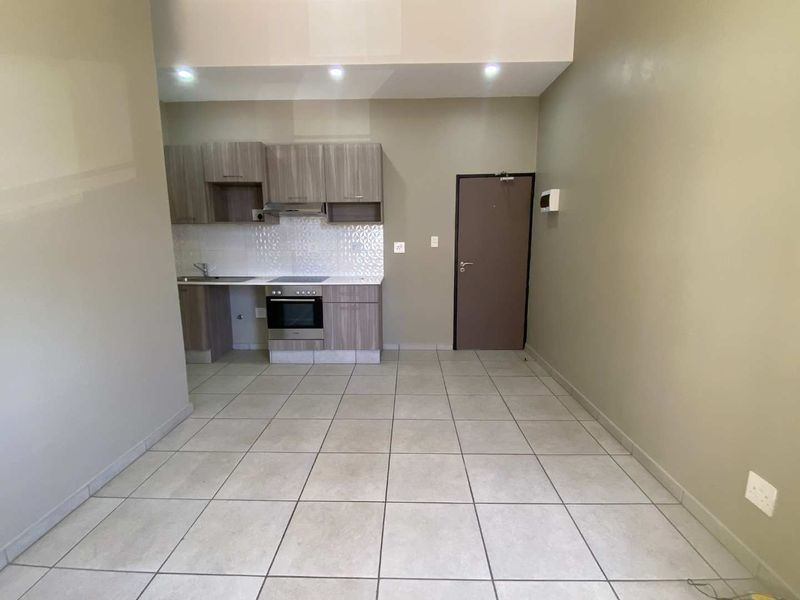 An open-plan living and kitchen area featuring modern built-in cabinetry, integrated appliances, tiled flooring, and recessed lighting in a clean, neutral space.