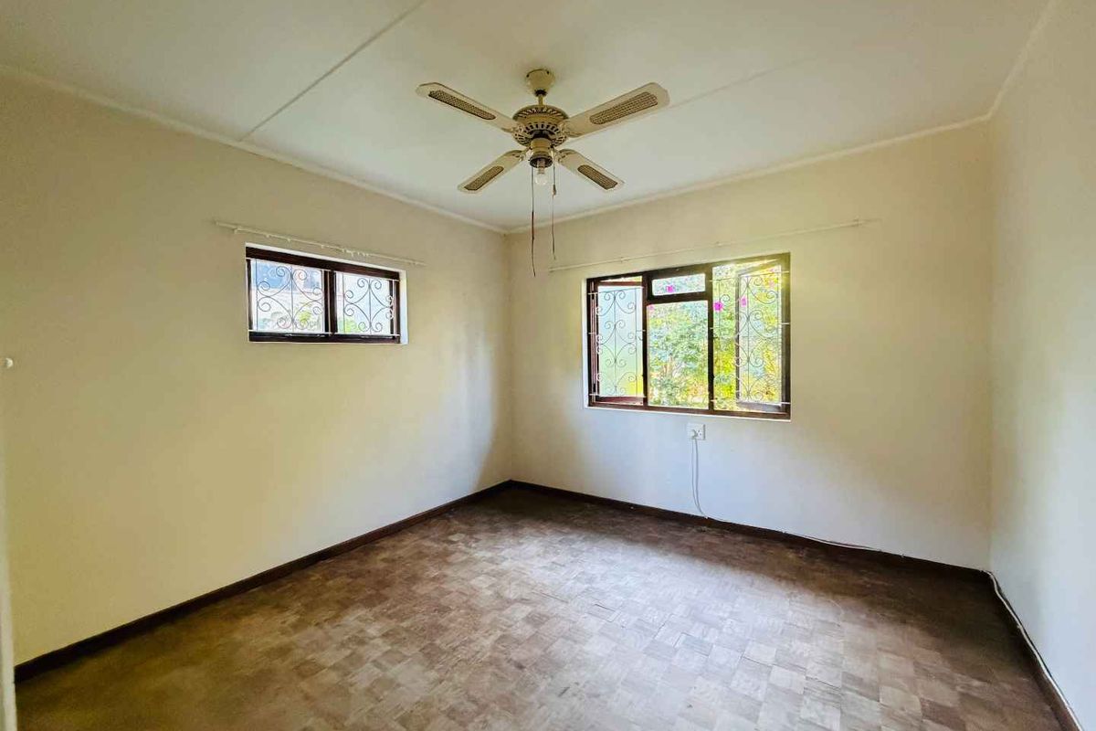 A bright, empty bedroom featuring tiled flooring, a ceiling fan, and security bars on the windows.