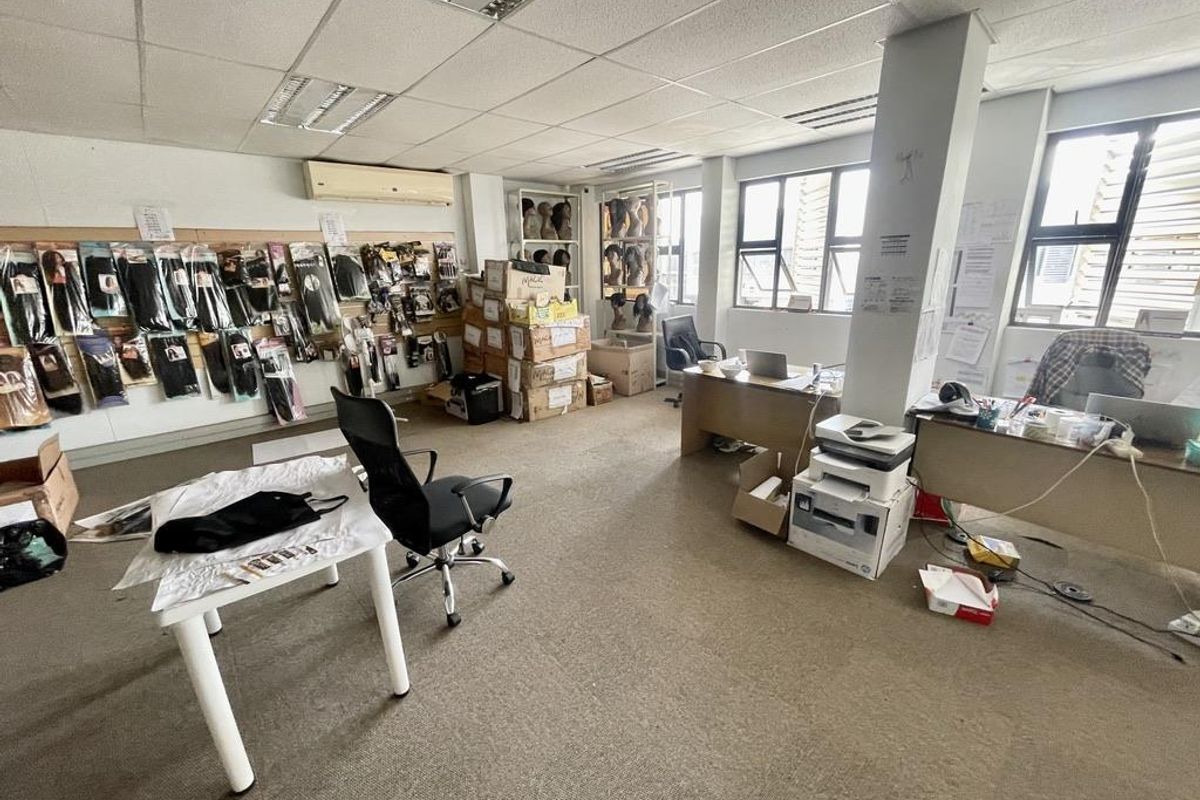 Open-plan office space featuring carpeted flooring, suspended ceiling with recessed lighting, wall-mounted air conditioning, and large windows providing natural light.