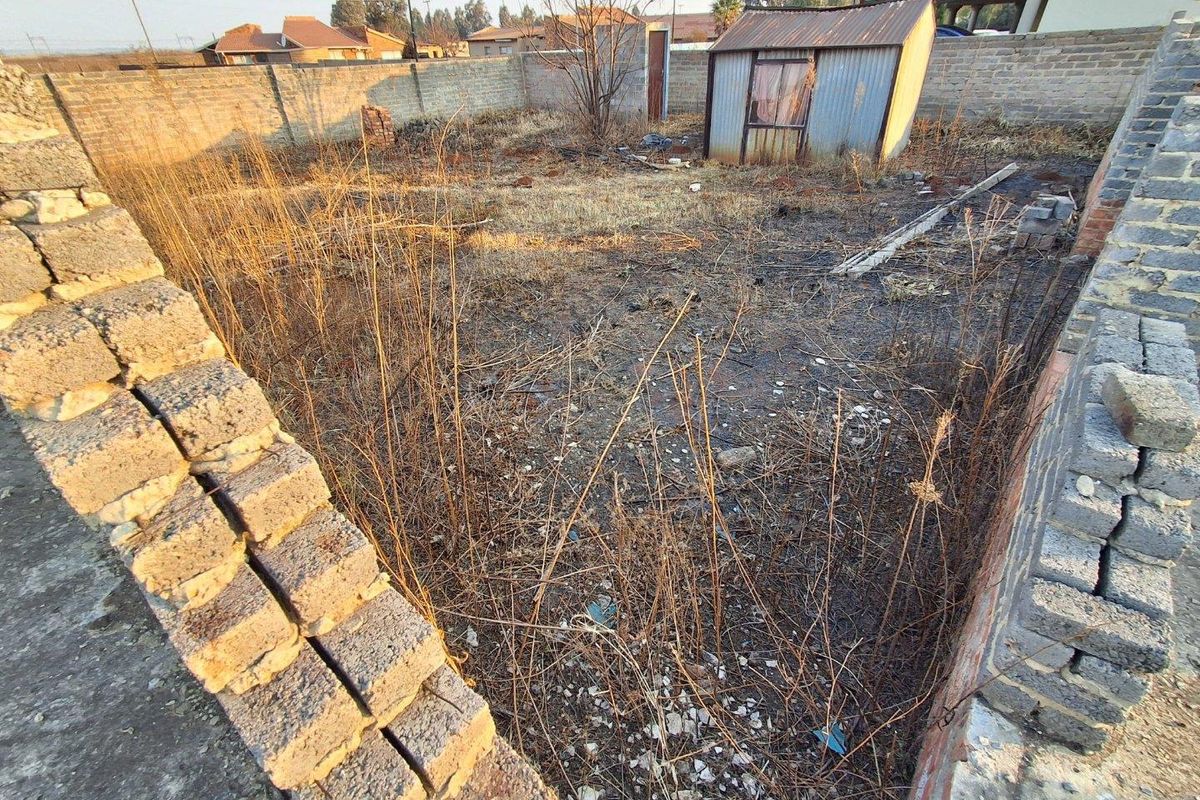 A vacant residential plot featuring a perimeter brick wall and an existing metal shed structure, requiring significant clearing and landscaping.