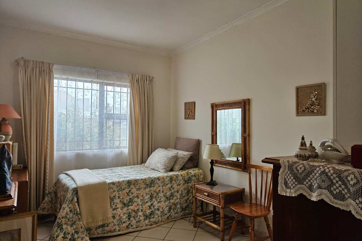 A functional bedroom featuring tiled flooring, a window with security bars, and neutral wall finishes, offering a comfortable and well-maintained living space.