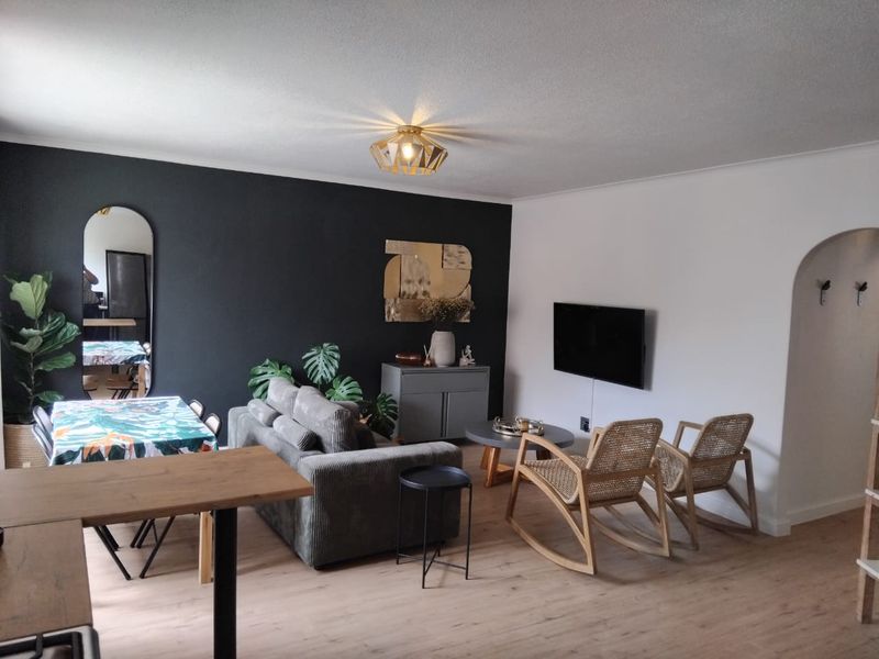 A well-maintained living room featuring light laminate flooring, a modern ceiling light fixture, and a distinctive arched doorway leading to adjacent spaces.