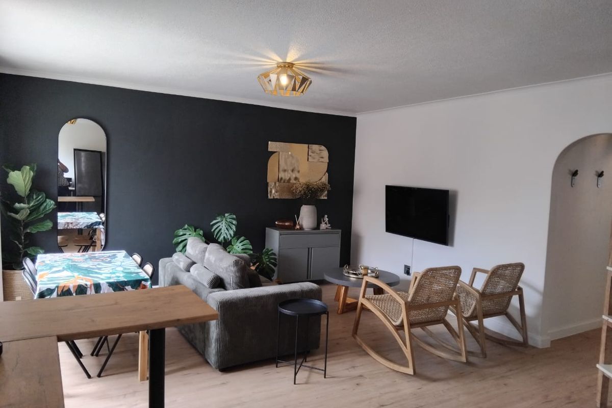 A well-maintained living room featuring light laminate flooring, a modern ceiling light fixture, and a distinctive arched doorway leading to adjacent spaces.