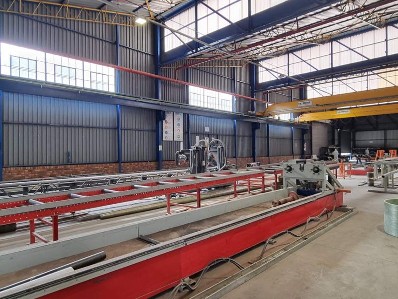 Spacious industrial warehouse facility featuring high ceilings, exposed steel trusses, overhead gantry cranes, and concrete flooring, suitable for manufacturing or storage operations.