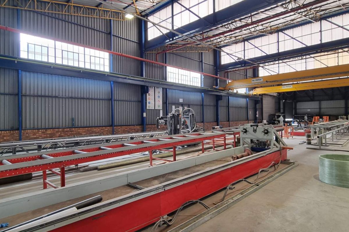 Spacious industrial warehouse facility featuring high ceilings, exposed steel trusses, overhead gantry cranes, and concrete flooring, suitable for manufacturing or storage operations.