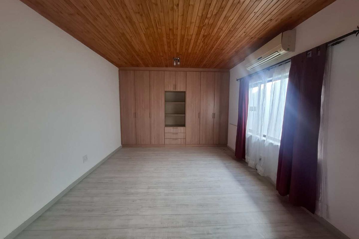 Spacious bedroom featuring light laminate flooring, a warm timber-paneled ceiling, extensive built-in cabinetry, and a wall-mounted air conditioning unit.