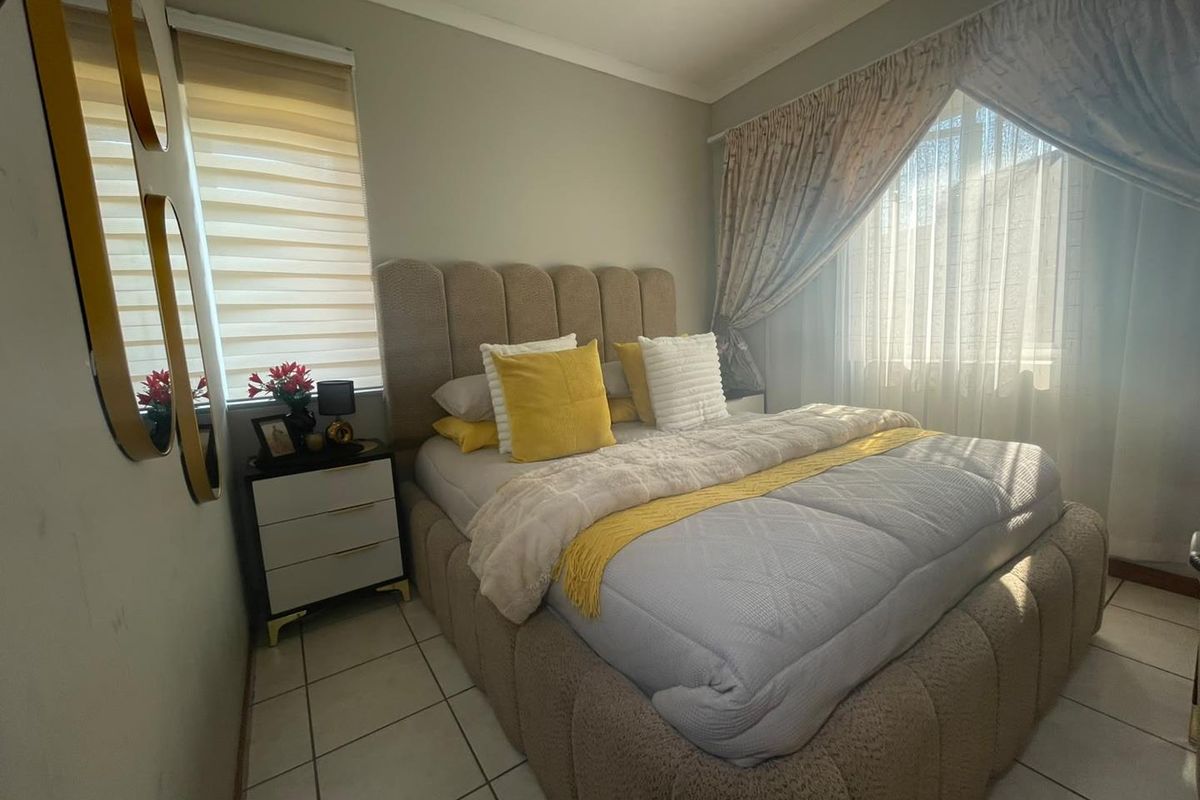 A well-lit bedroom featuring tiled flooring, neutral wall finishes, and window treatments including roller blinds and curtain rails.