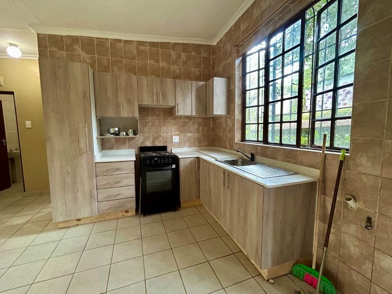 A functional kitchen featuring light wood-finish cabinetry, tiled walls, and a stainless steel sink, offering a clean and practical workspace.