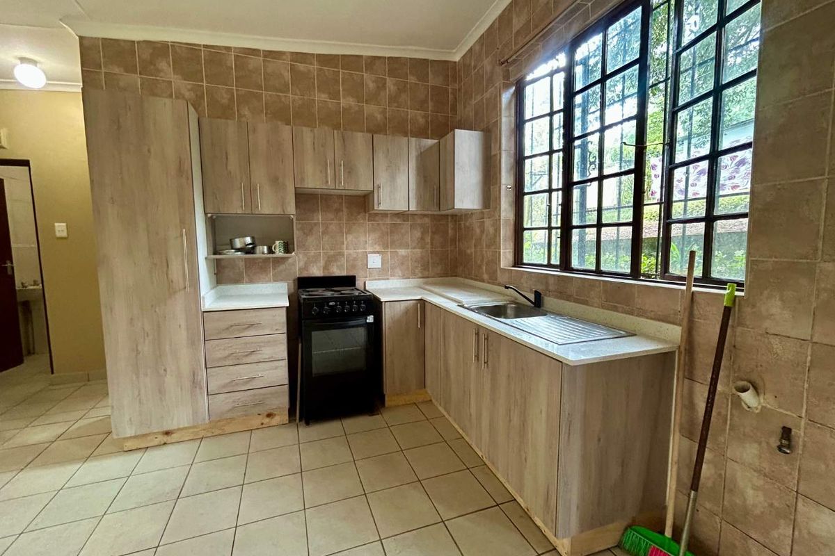 A functional kitchen featuring light wood-finish cabinetry, tiled walls, and a stainless steel sink, offering a clean and practical workspace.