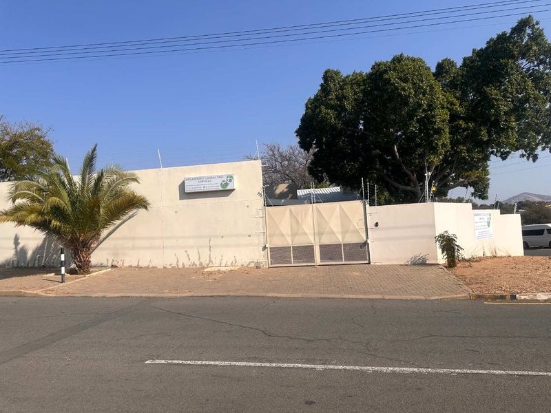 Front exterior view of a business property featuring a perimeter wall with electric fencing, a metal security gate, and paved driveway access.