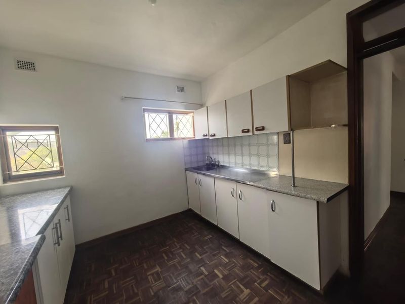 A dated kitchen featuring parquet flooring, laminate countertops, built-in cabinetry, and a stainless steel sink, offering potential for a modern renovation.