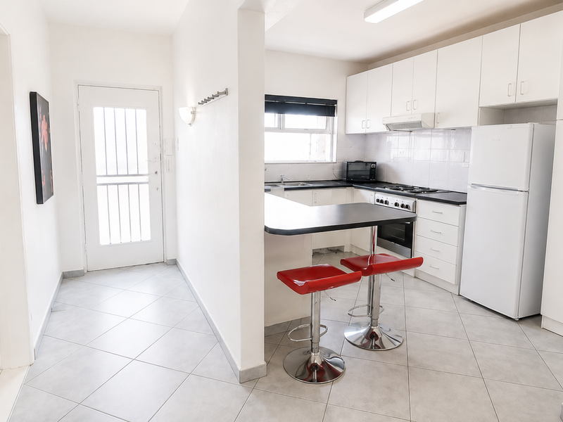 Open-plan kitchen featuring white cabinetry, dark countertops, built-in appliances, and tiled flooring, seamlessly connected to the entrance area.