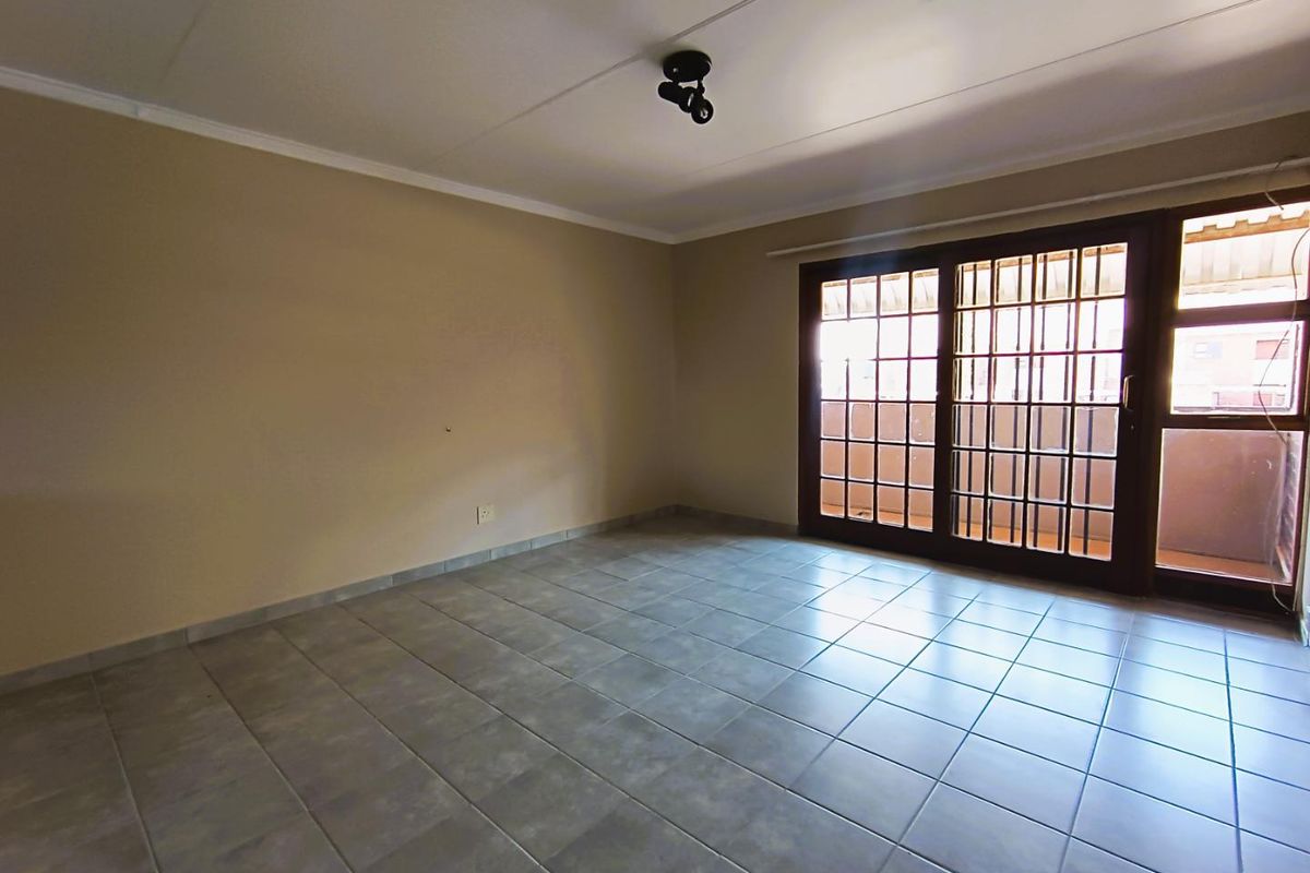 An empty living room featuring tiled flooring, neutral walls, and sliding glass doors with security bars leading to an outdoor area.