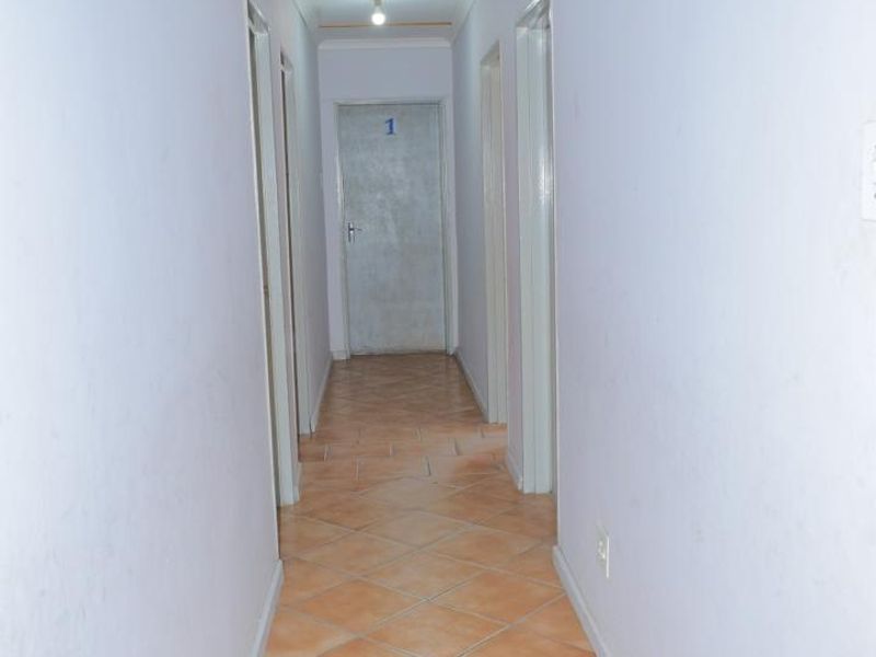 A long, empty residential hallway featuring tiled flooring and multiple internal doors, providing access to various rooms within the property.