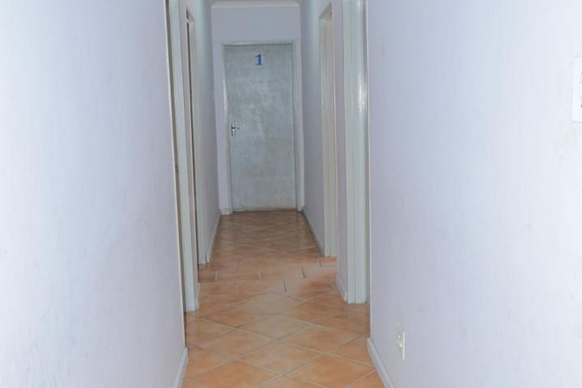 A long, empty residential hallway featuring tiled flooring and multiple internal doors, providing access to various rooms within the property.