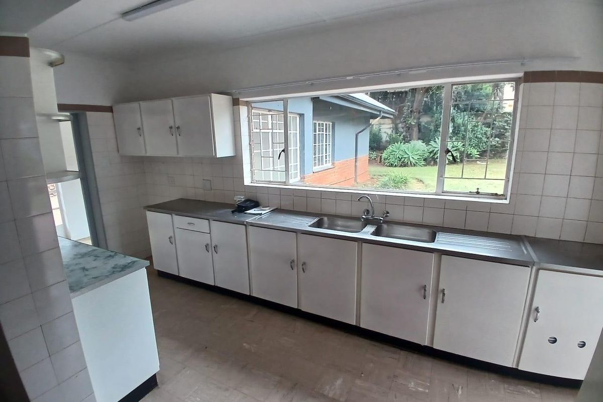 A functional kitchen featuring white cabinetry, stainless steel double sink, and tiled splashbacks with a view overlooking the garden.