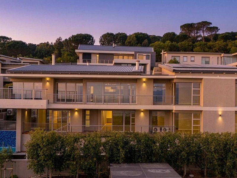A modern multi-level residential property featuring expansive balconies, large sliding glass doors, solar panels, and a private swimming pool at dusk.
