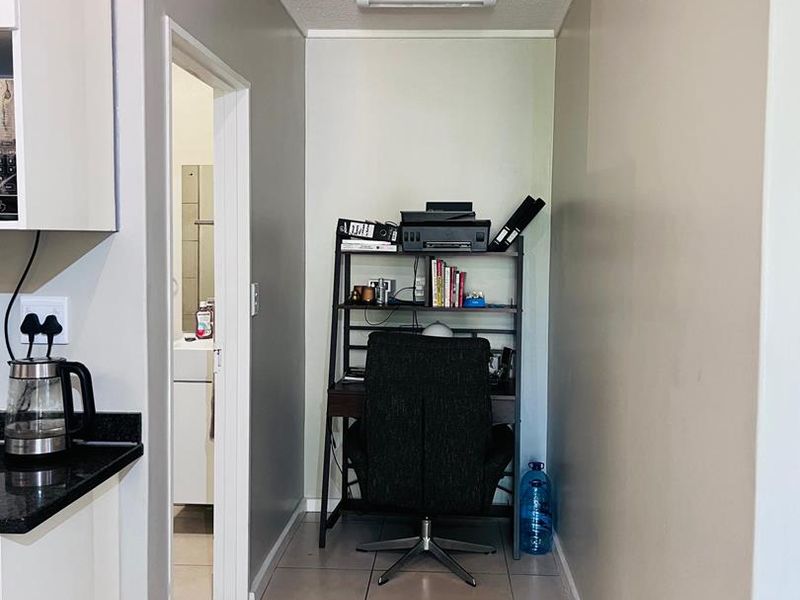 A compact office nook featuring tiled flooring and neutral walls, conveniently located adjacent to the kitchen area.