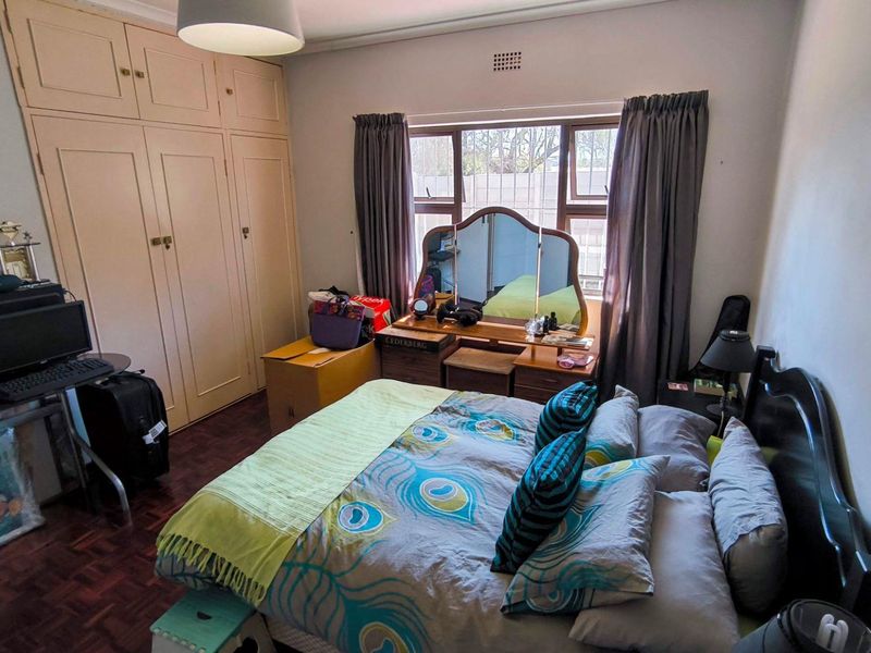 A bedroom featuring parquet flooring and built-in cupboards, offering a functional space with natural light from the window.