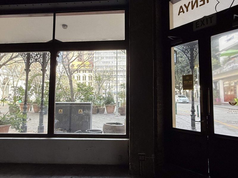Interior view of a retail entrance featuring large display windows, glass door, and exposed brickwork, offering a view of the street and plaza.
