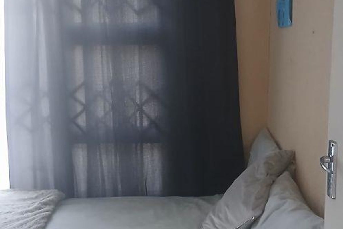 A compact bedroom featuring a window with security bars and neutral wall tones, providing a functional sleeping space.
