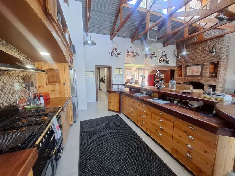 Spacious open-plan kitchen and living area featuring exposed timber roof trusses, extensive wooden cabinetry, a breakfast bar, and a prominent brick fireplace.
