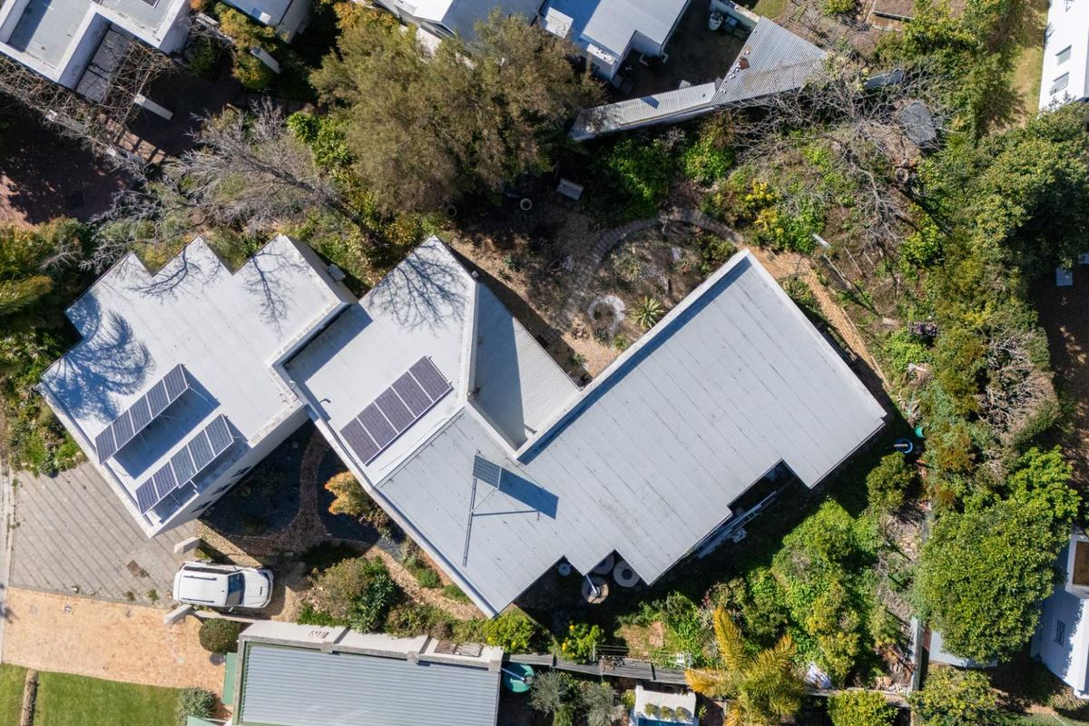 Aerial view of the property showcasing the roof structure, installed solar panels, and surrounding landscaped garden area.
