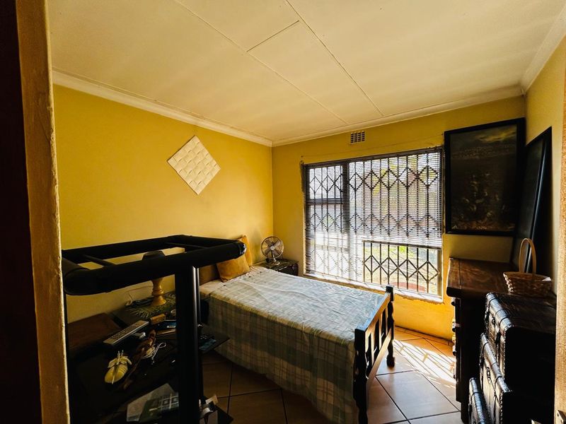 A bedroom featuring tiled flooring, a window with a security gate, and ceiling cornice detailing.