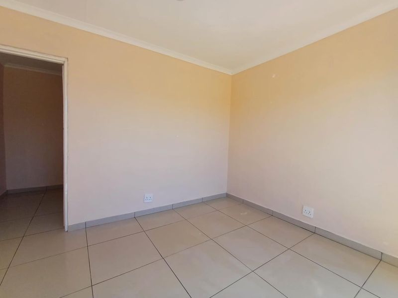 A clean, empty bedroom featuring neutral wall paint, tiled flooring, and standard electrical fixtures, offering a blank canvas for personalization.