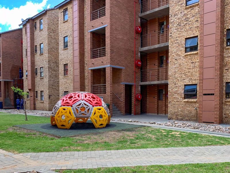 Exterior view of a multi-story face brick apartment complex featuring communal lawn areas, paved pathways, and integrated fire safety infrastructure.