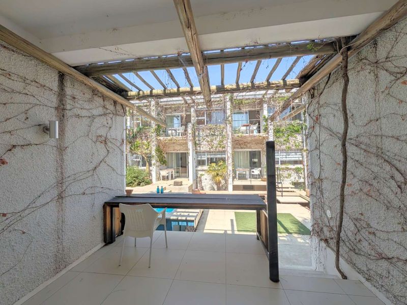 Covered patio area featuring a timber pergola structure, tiled flooring, and textured walls, overlooking a central courtyard and pool area.