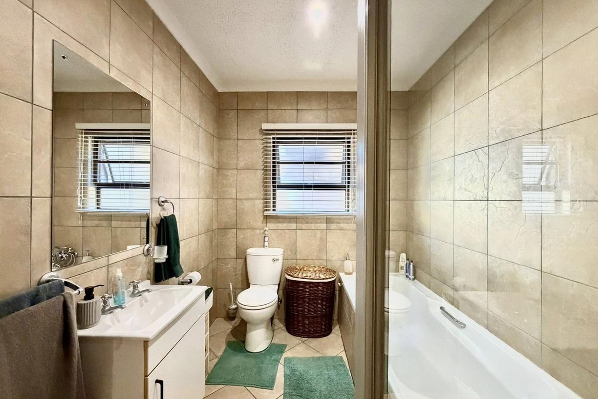 A functional bathroom featuring a built-in vanity, a standard toilet, and a bathtub with a glass shower screen, finished with neutral wall and floor tiles.