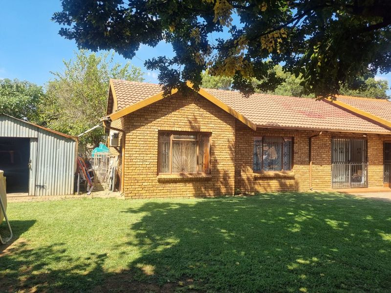 Rear view of a face brick house featuring a tiled roof, security gates, and a detached metal garden shed set within a lawned garden.