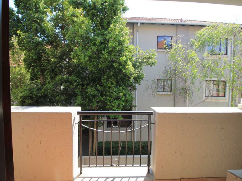 A private balcony featuring a metal balustrade and tiled flooring, overlooking the apartment complex grounds and mature trees.