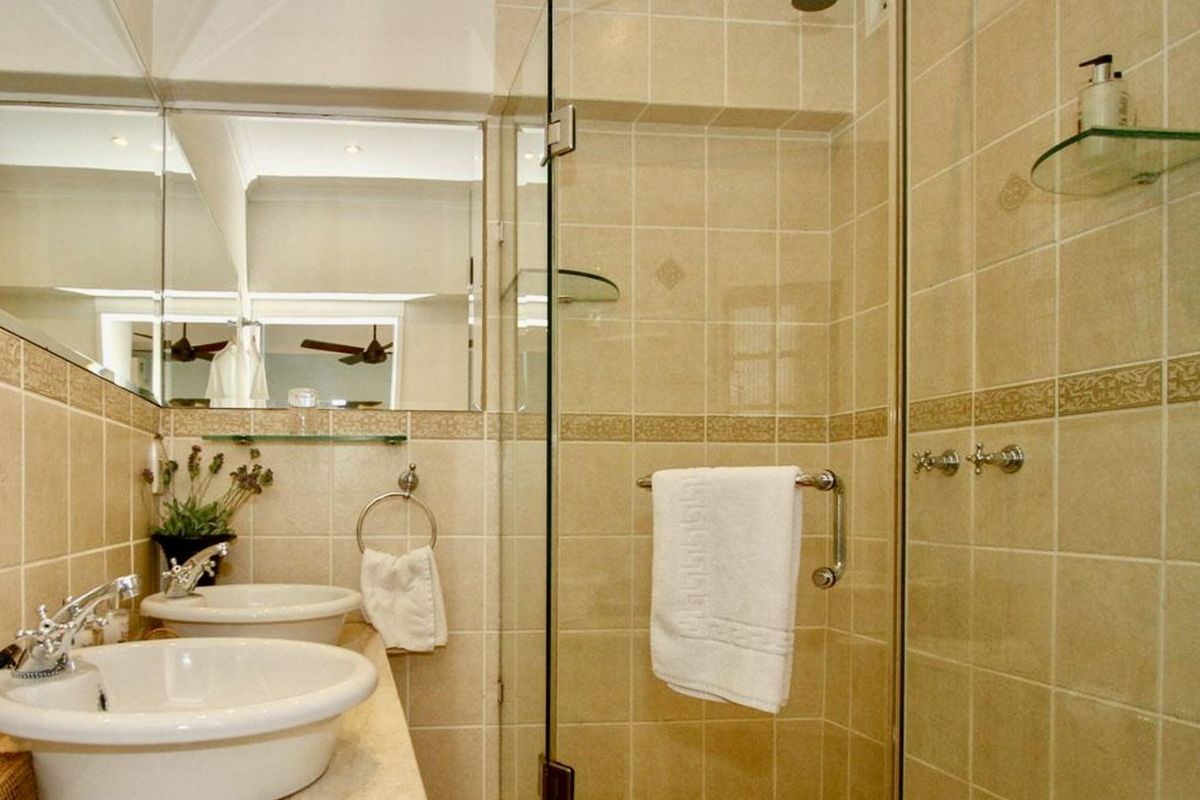 A functional bathroom featuring a double vanity with ceramic basins, a glass-enclosed shower, and neutral wall tiling.