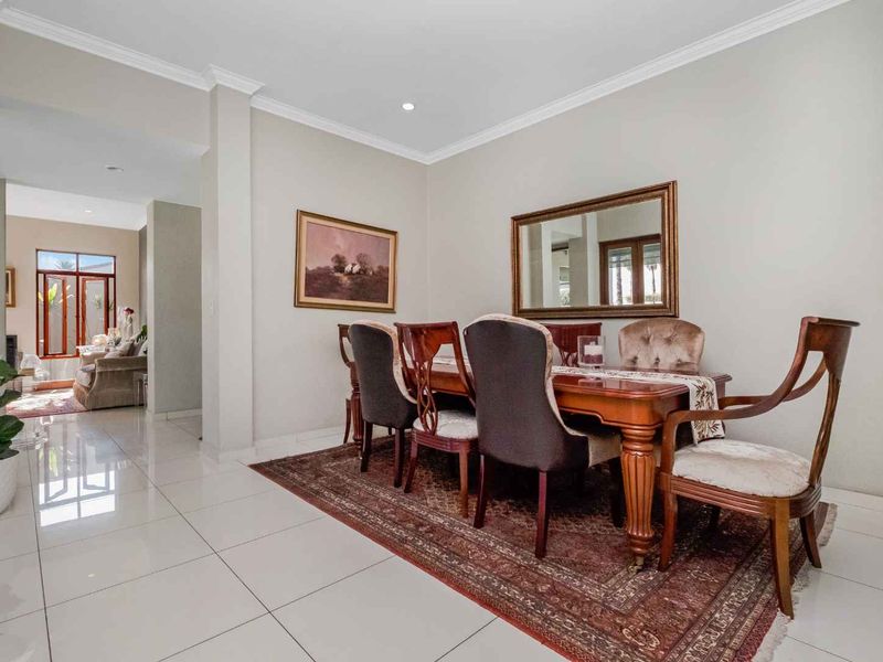 A bright dining room featuring polished porcelain floor tiles, recessed downlighting, and elegant cove cornicing, creating a clean and well-maintained living space.