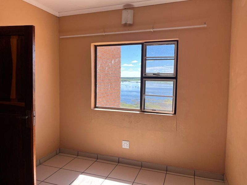 An empty bedroom featuring tiled flooring, a timber door, and a window offering scenic water views.