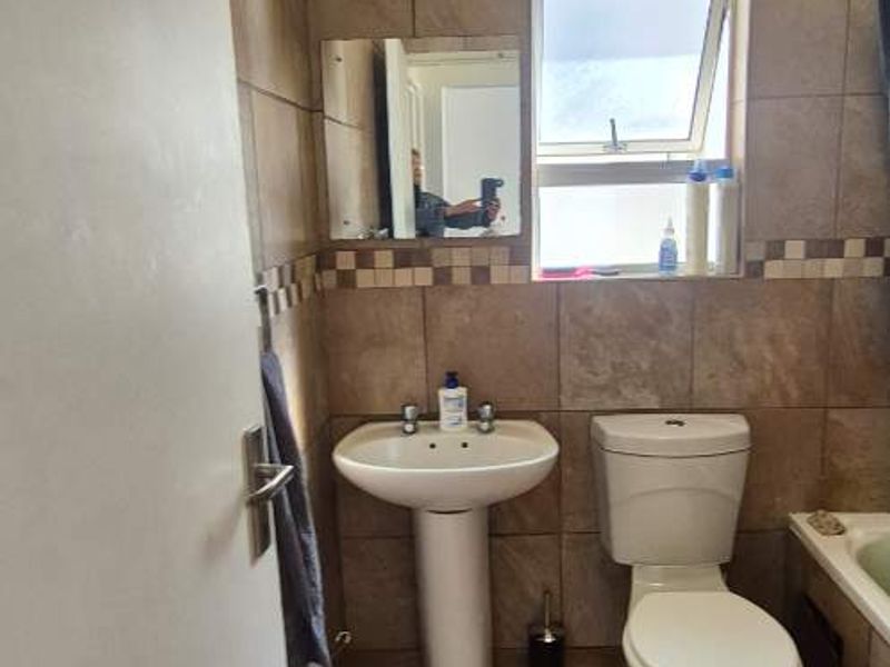 A functional bathroom featuring a pedestal washbasin, toilet, and full-height wall tiling with a decorative border.