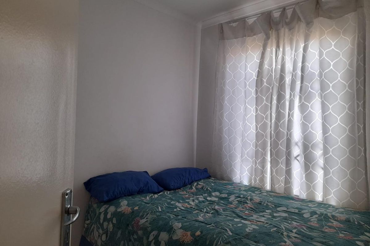 A compact bedroom featuring a window with curtains and neutral wall finishes.
