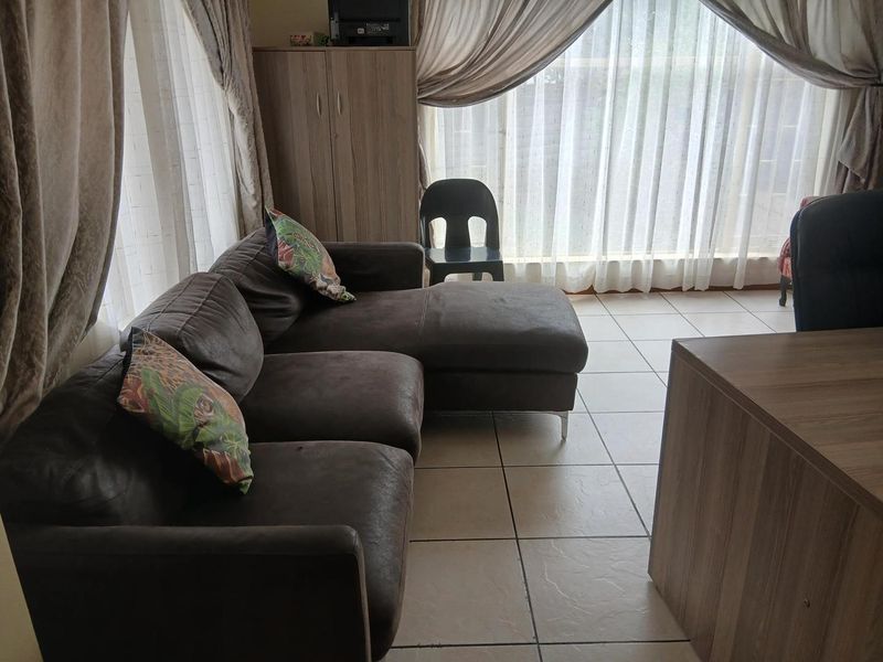 A living room area featuring tiled flooring and large windows with curtains, providing natural light to the space.