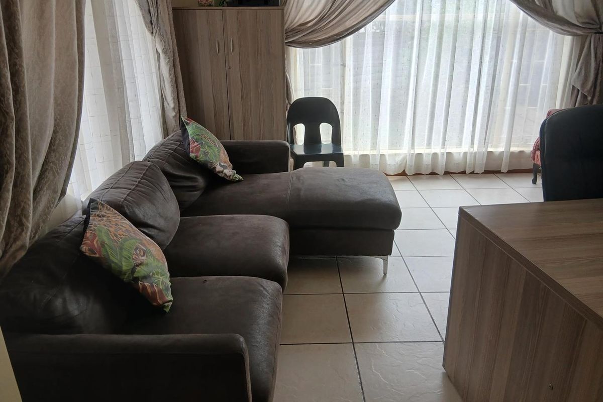 A living room area featuring tiled flooring and large windows with curtains, providing natural light to the space.