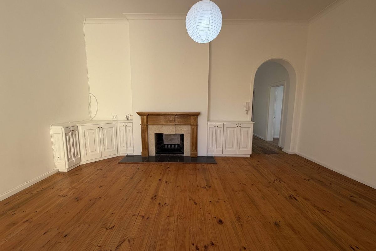 Spacious living room featuring polished timber flooring, a central fireplace with built-in cabinetry, and an elegant arched doorway leading to the hallway.