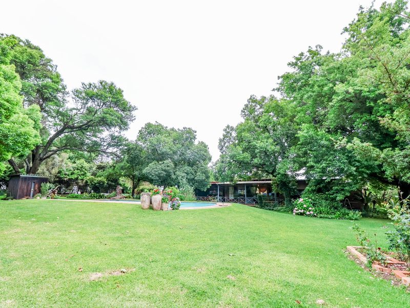 A spacious rear garden featuring a well-maintained lawn, mature trees, and a swimming pool area with a covered patio.