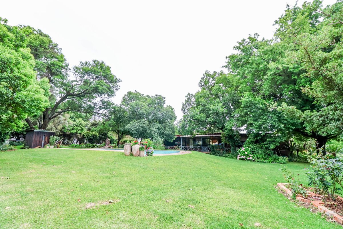 A spacious rear garden featuring a well-maintained lawn, mature trees, and a swimming pool area with a covered patio.